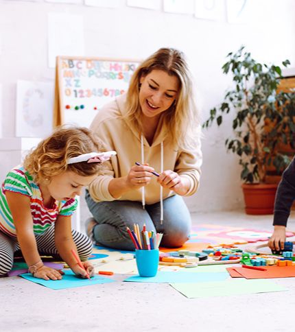 Children drawing and building with colourful blocks alongside a carer